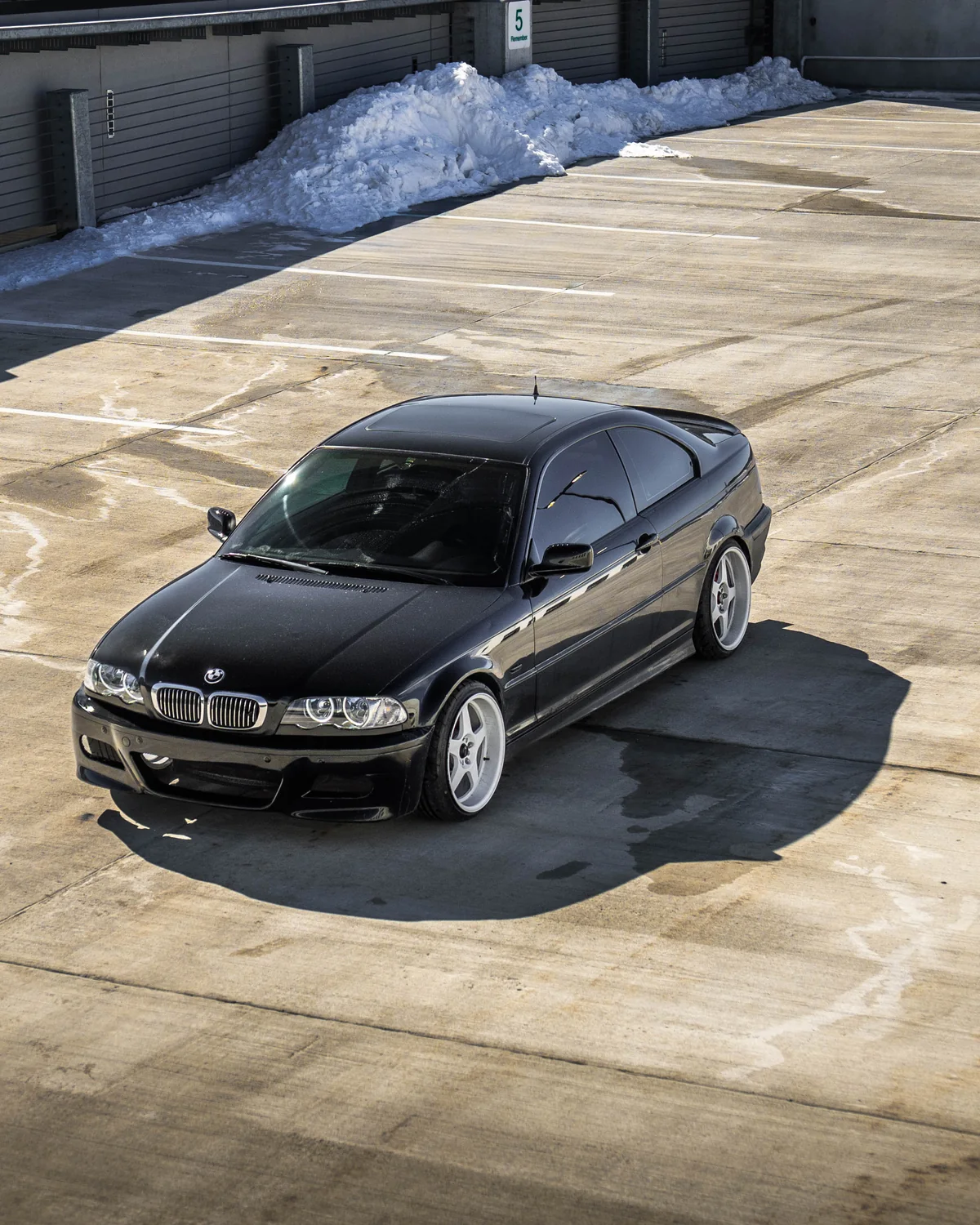 Alex's own black BMW E46 build on white wheels, shot from above in a sunlit concrete lot