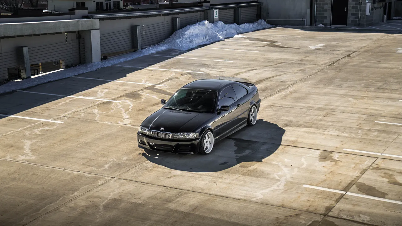 Black BMW E46 coupe shot from above on an open concrete rooftop parking deck