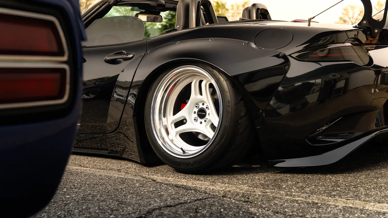 Close low view of a black widebody car's rear wheel with a white deep-dish rim and red brake caliper