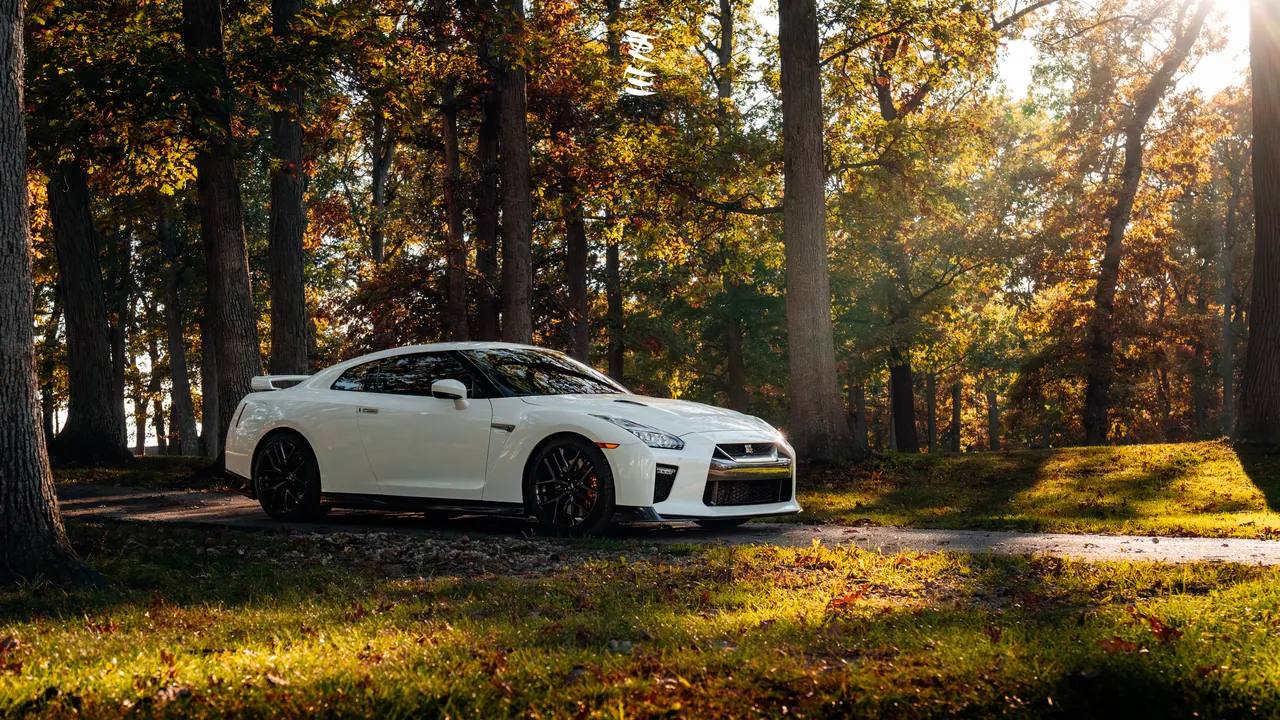 White Nissan GT-R R35 parked in an autumn forest with warm light filtering through the trees