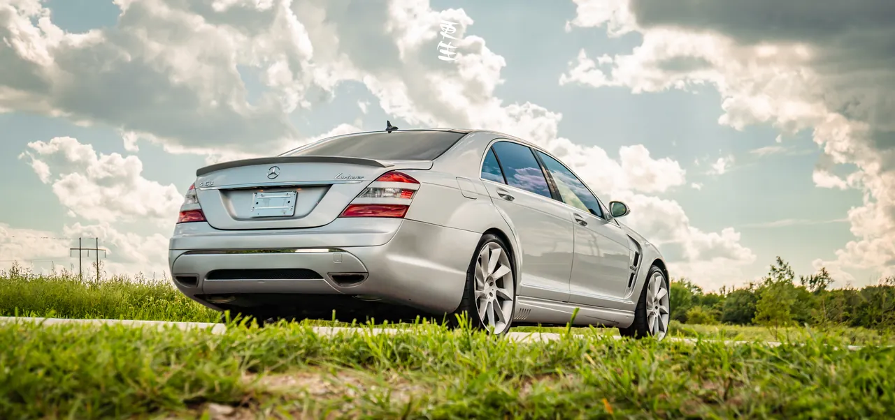 Silver Mercedes-Benz sedan shot from the rear three-quarter against a dramatic cloudy sky