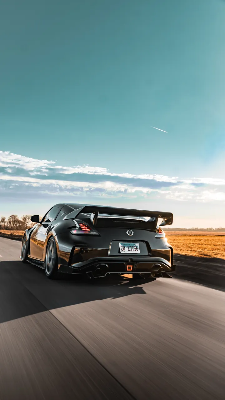 Black Nissan Z sports car with a rear wing captured in motion on an open highway at golden hour