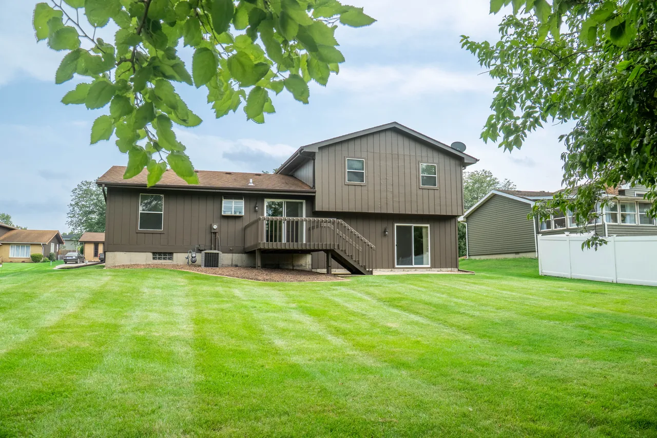 Rear of the home seen across a striped, freshly mown backyard framed by overhanging tree branches
