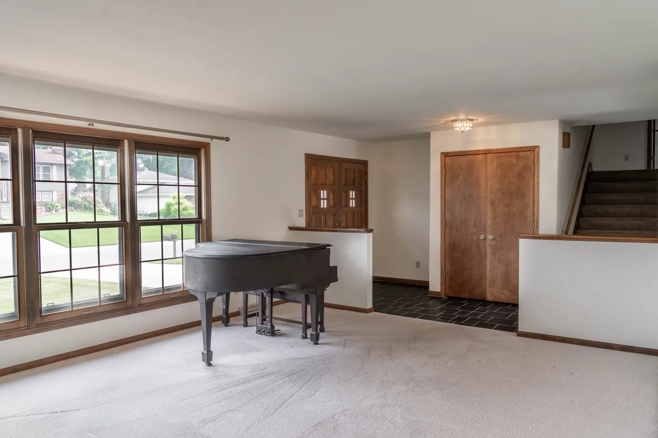 Living room with a wall of windows, a grand piano and an open stairway beyond