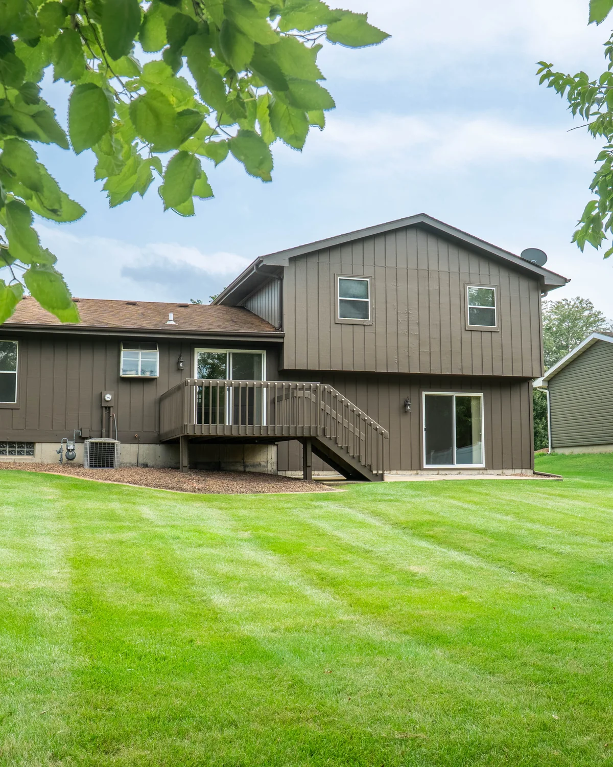 Rear of a suburban home framed by overhanging tree branches above a freshly mown, striped lawn